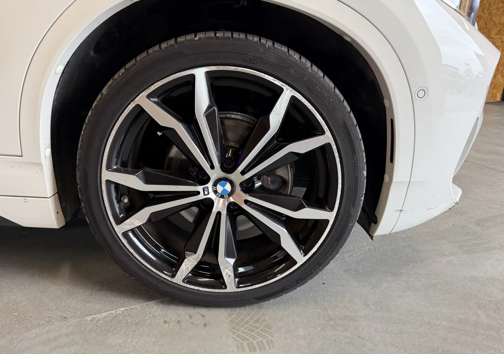 Gros plan sur la roue avant droite d'une BMW X2 blanche avec jante alu 19'' bicolore et logo BMW central.
