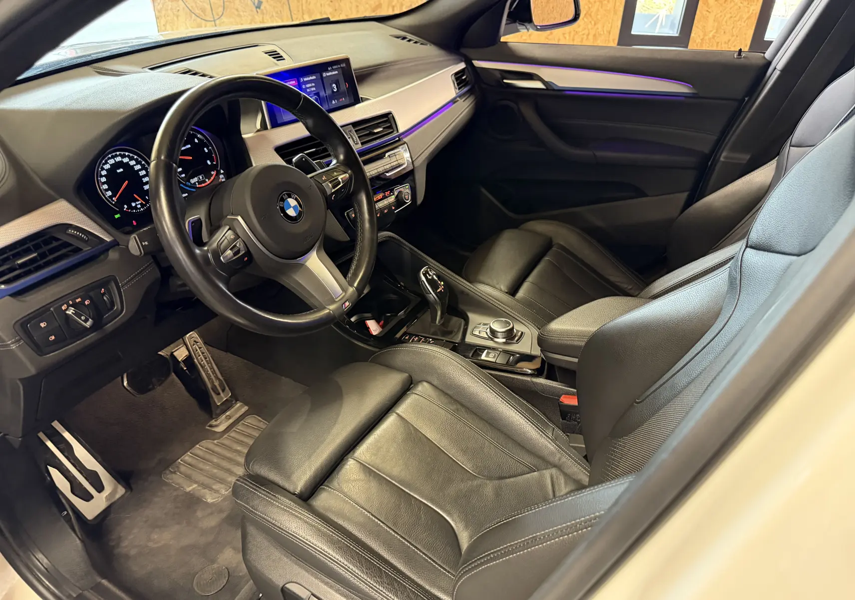 Intérieur noir cuir M Sport de BMW X2 sDrive18d 2023 vu côté conducteur, avec volant multifonctions et éclairage d'ambiance violet.