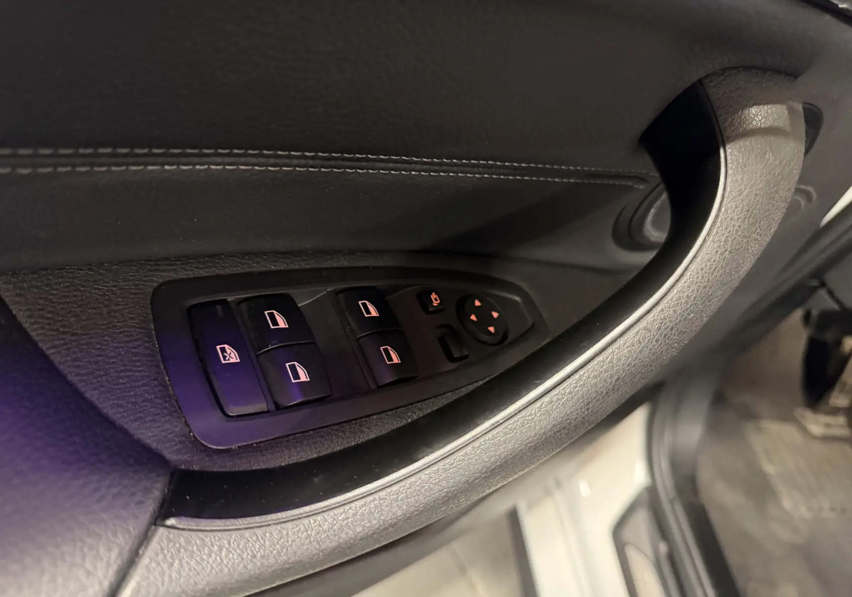Gros plan sur les commandes électriques des vitres et rétroviseurs sur la porte côté conducteur d’une BMW X2 blanche.