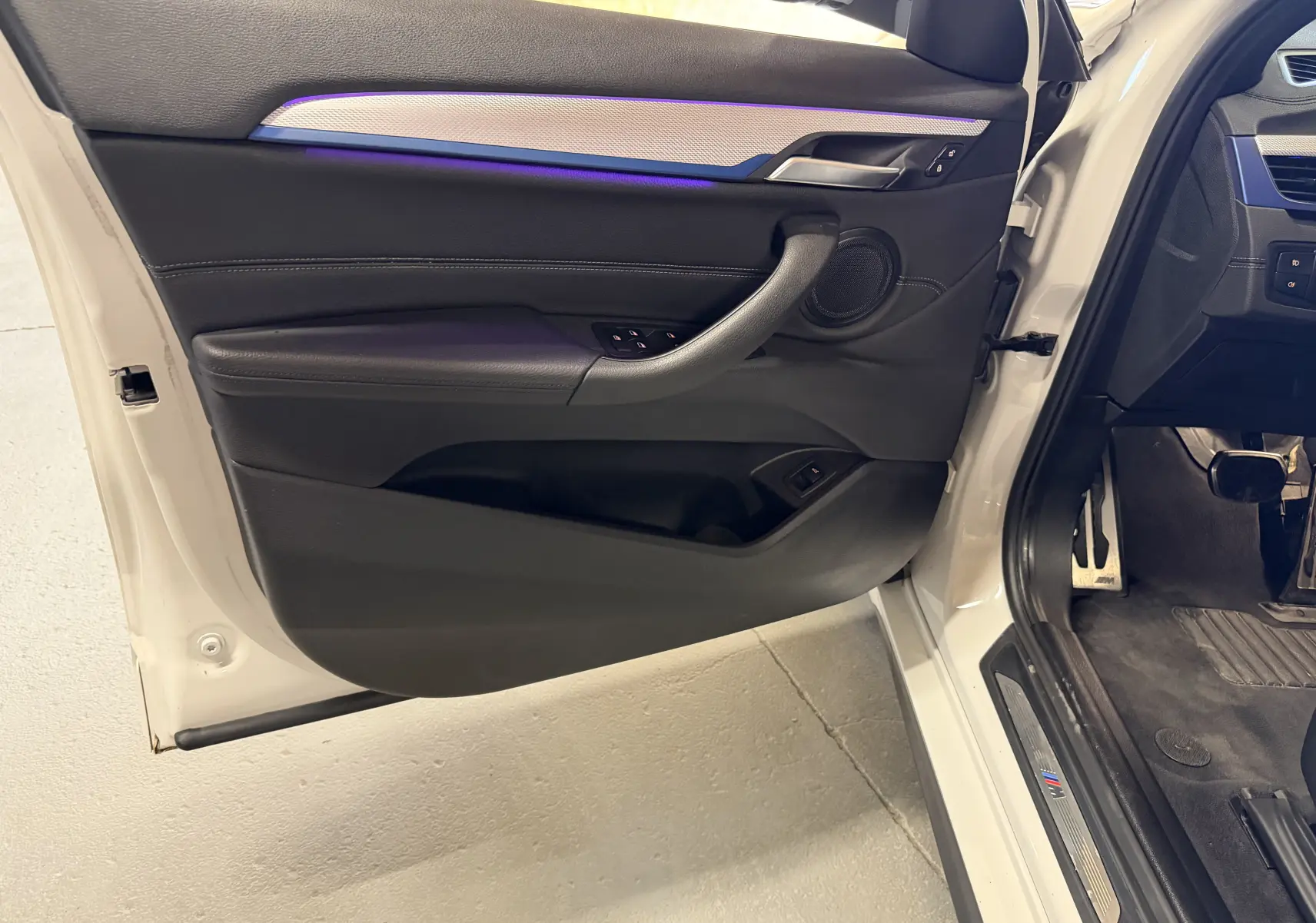 Vue intérieure de la porte avant gauche blanche d’un BMW X2 2023 avec éclairage d’ambiance violet et garniture noire.