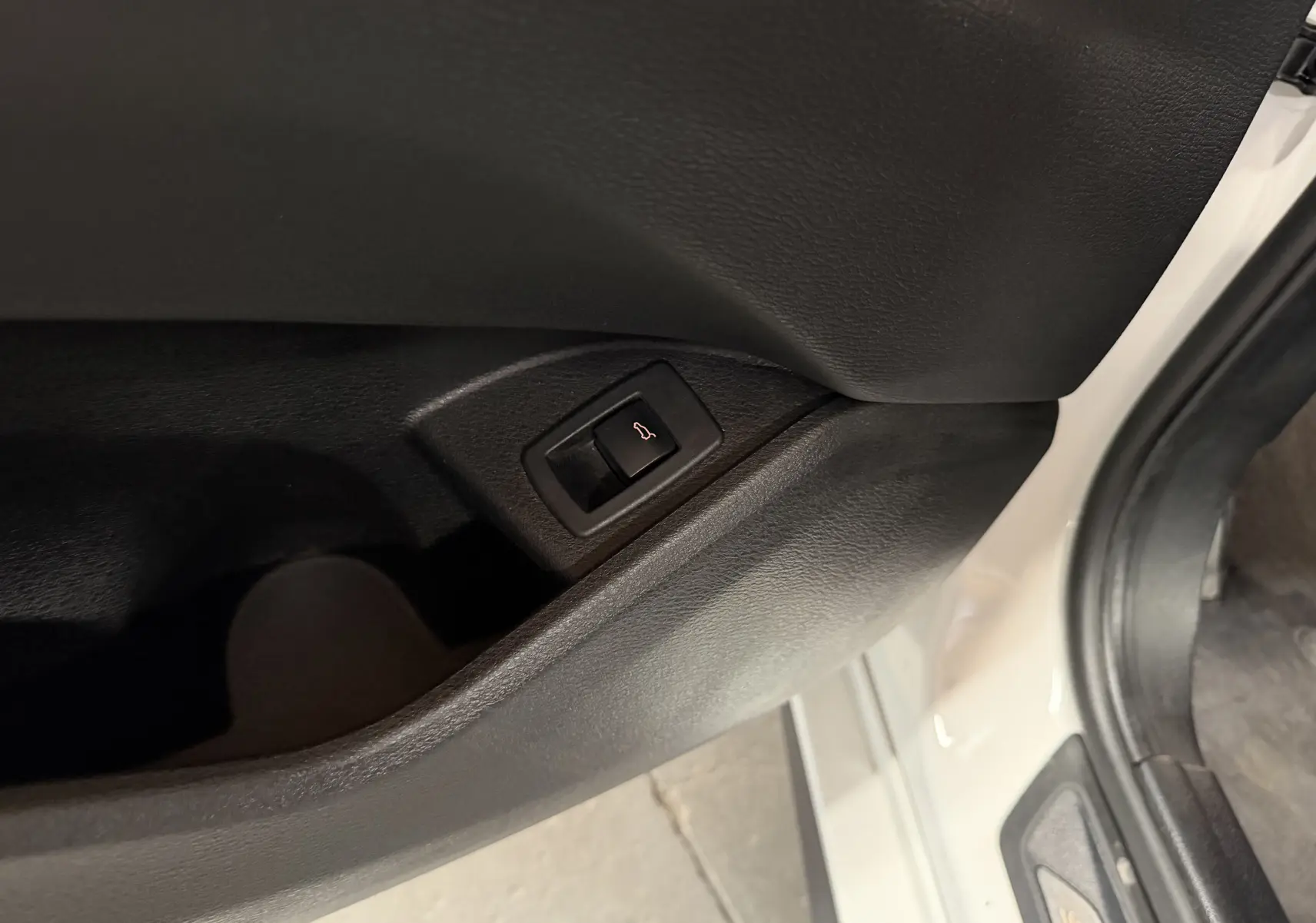 Gros plan sur le bouton d'ouverture électrique du hayon, sur la porte côté gauche d'un BMW X2 blanc.