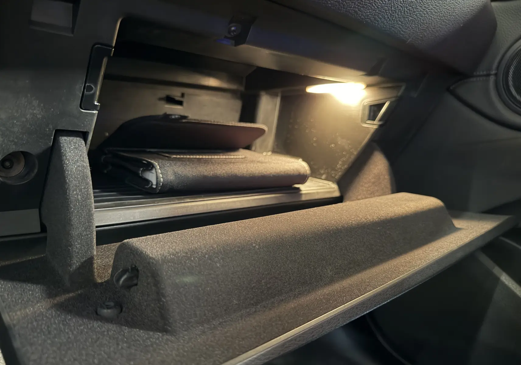 Vue rapprochée de la boîte à gants ouverte du BMW X2 blanc 2023, éclairée avec un manuel à l'intérieur.