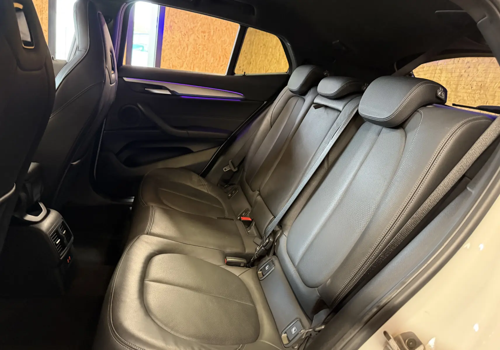 Vue intérieure côté droit des sièges arrière en cuir noir du BMW X2 sDrive18d blanc, avec habillage de porte et ceintures visibles.