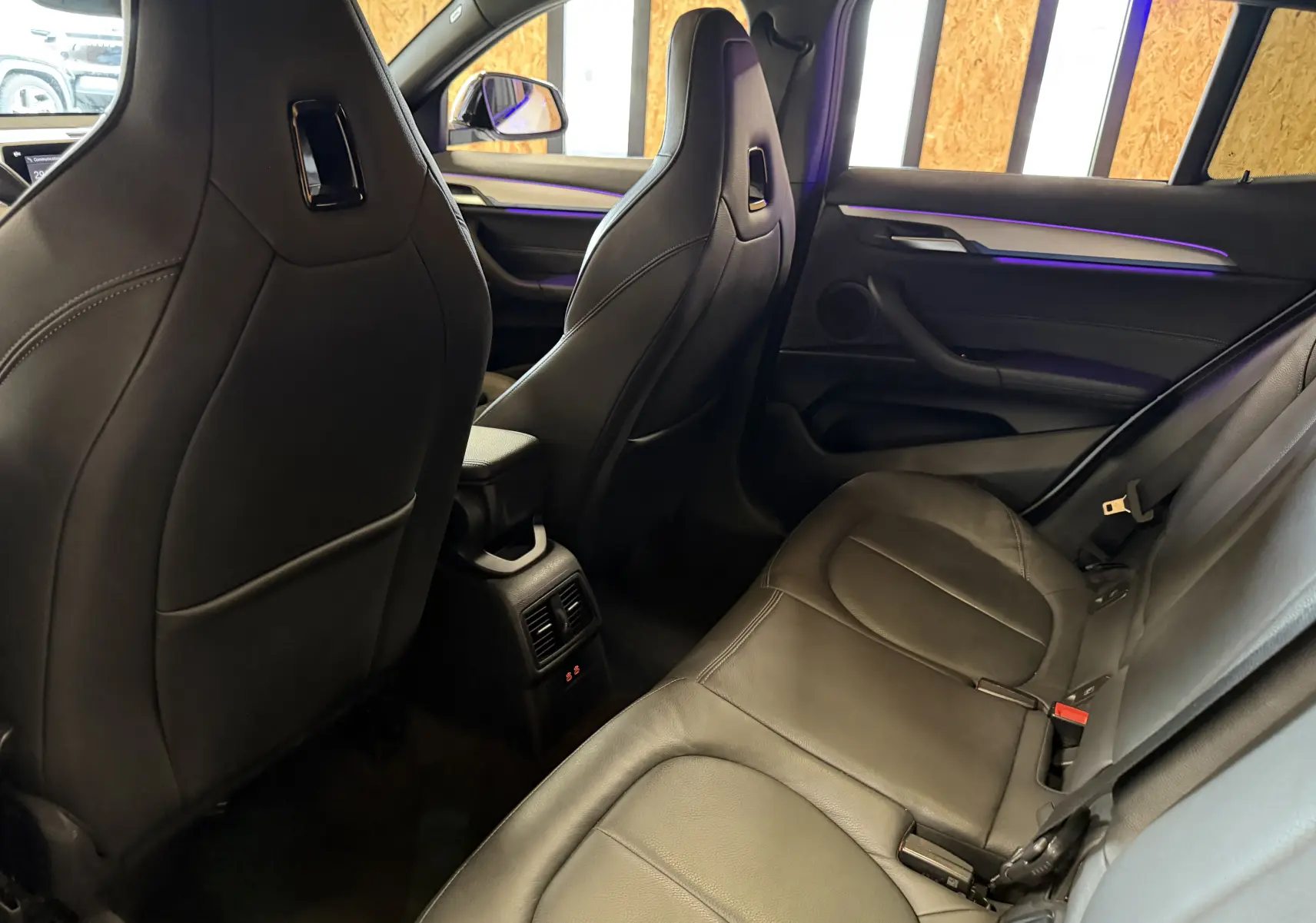 Vue intérieure arrière côté droit du BMW X2 sDrive18d 2023 avec sièges en cuir noir et éclairage d'ambiance violet.