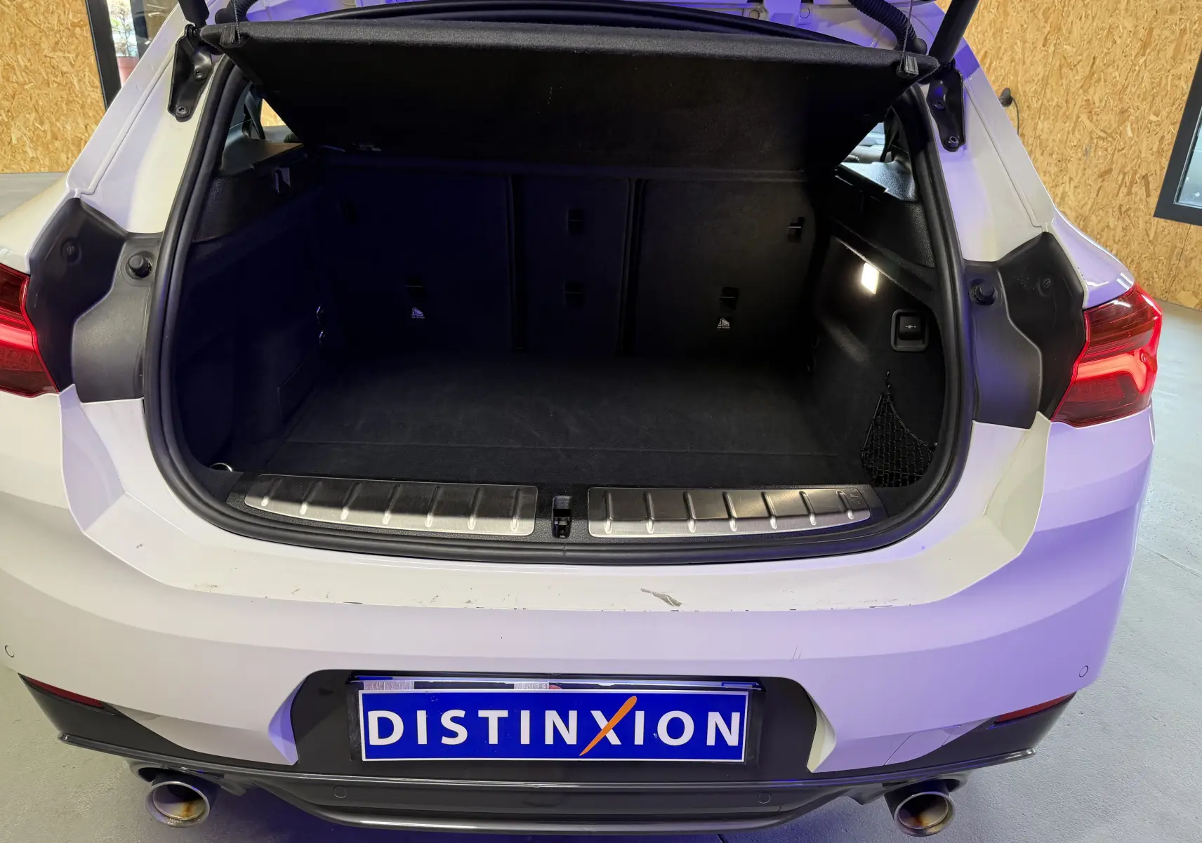 Coffre ouvert vu de l'arrière d'un BMW X2 blanc avec seuil de chargement inox et sorties d'échappement chromées.