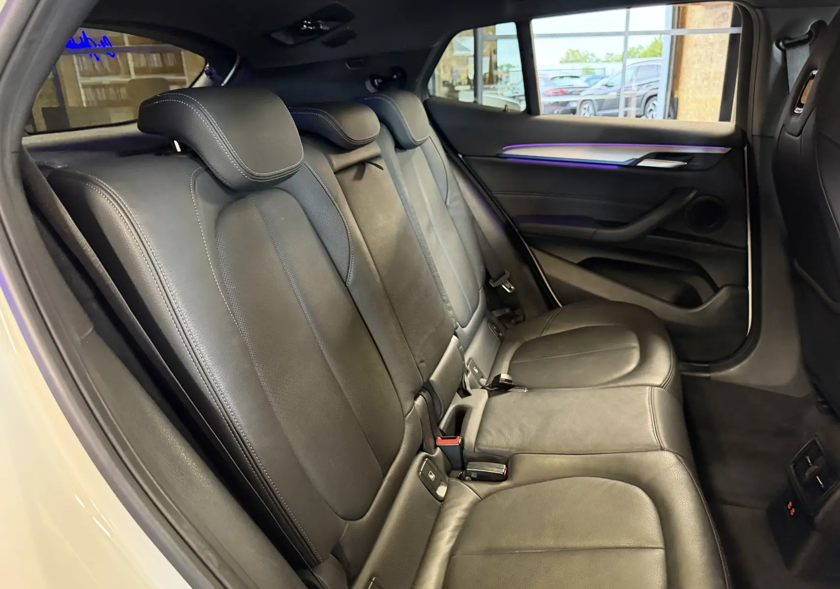 Vue intérieure côté droit des sièges arrière en cuir noir avec éclairage d'ambiance violet dans une BMW X2 blanche.