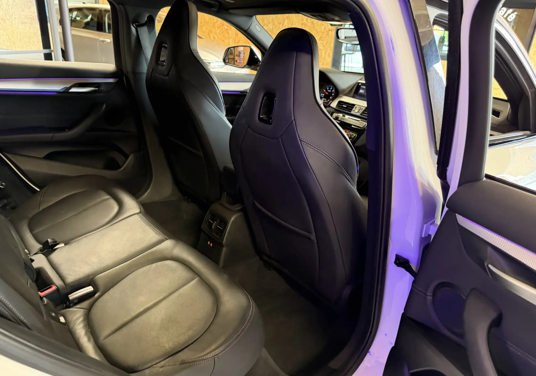 Vue intérieure côté gauche montrant les sièges arrière et avant noirs en cuir avec détails modernes sur BMW X2 blanc.