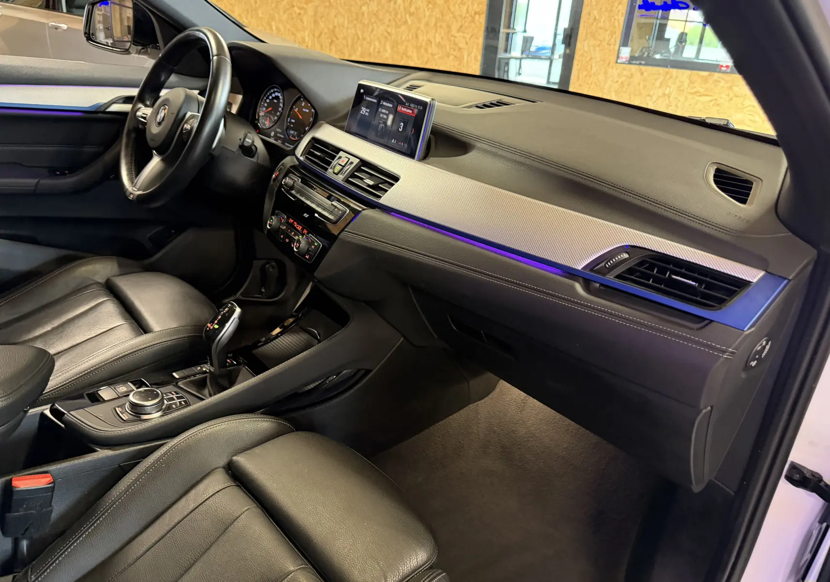 Intérieur BMW X2 sDrive18d 2023 vu côté conducteur, tableau de bord noir avec éclairage d'ambiance violet.