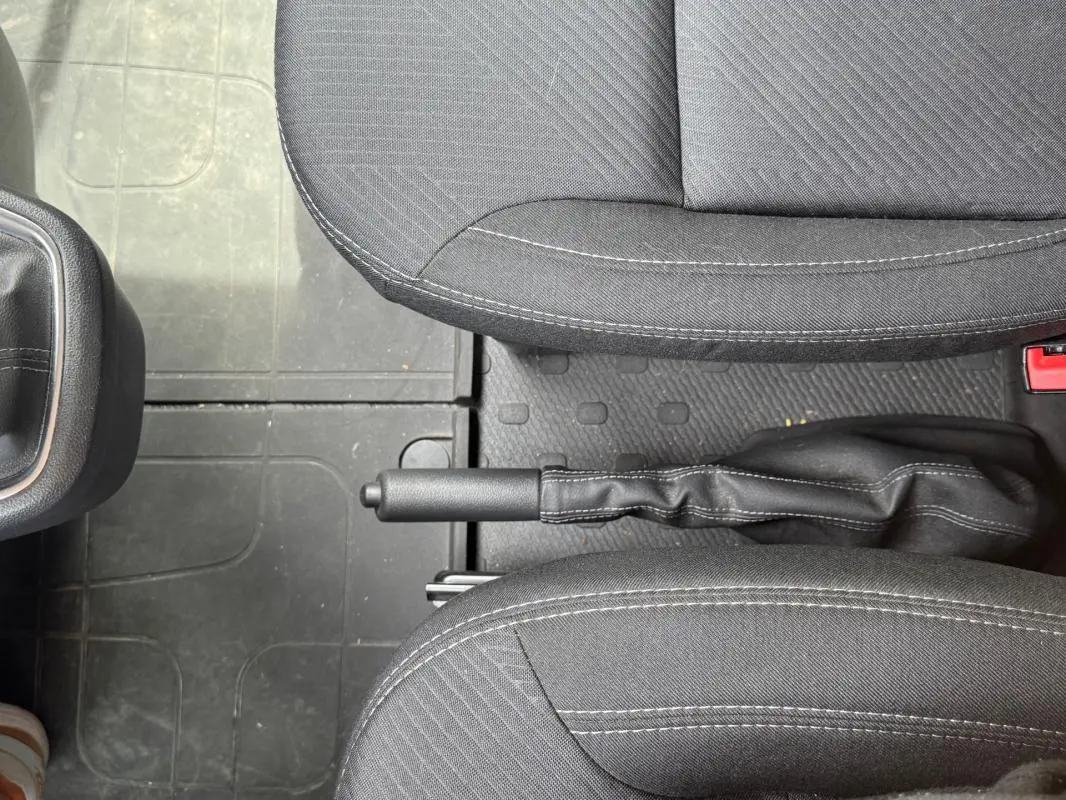 Vue intérieure centrée sur le frein à main entre les sièges avant en tissu gris foncé du Renault Trafic Fourgon 2024.