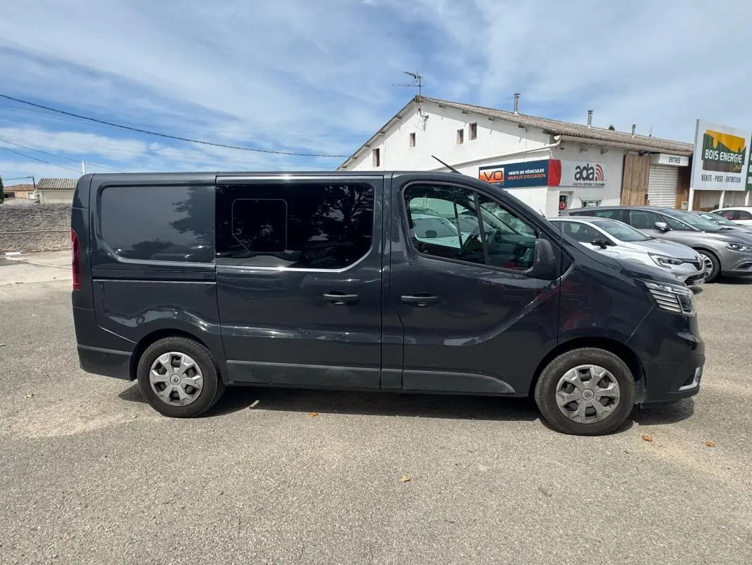 Vue de profil côté gauche d'un Renault Trafic Fourgon gris foncé avec vitres surteintées et porte latérale.