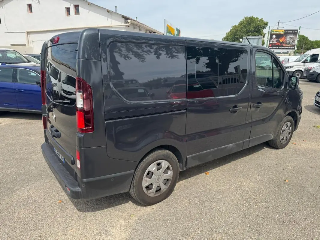 Renault Trafic Fourgon gris foncé vu en 3/4 arrière droit, avec porte latérale et vitres surteintées.