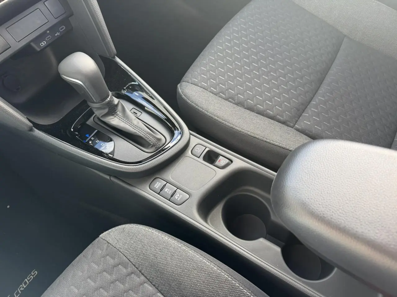 Vue intérieure centrée sur la console centrale et levier de vitesse automatique, sièges tissu gris foncé de la Toyota Yaris Cross.
