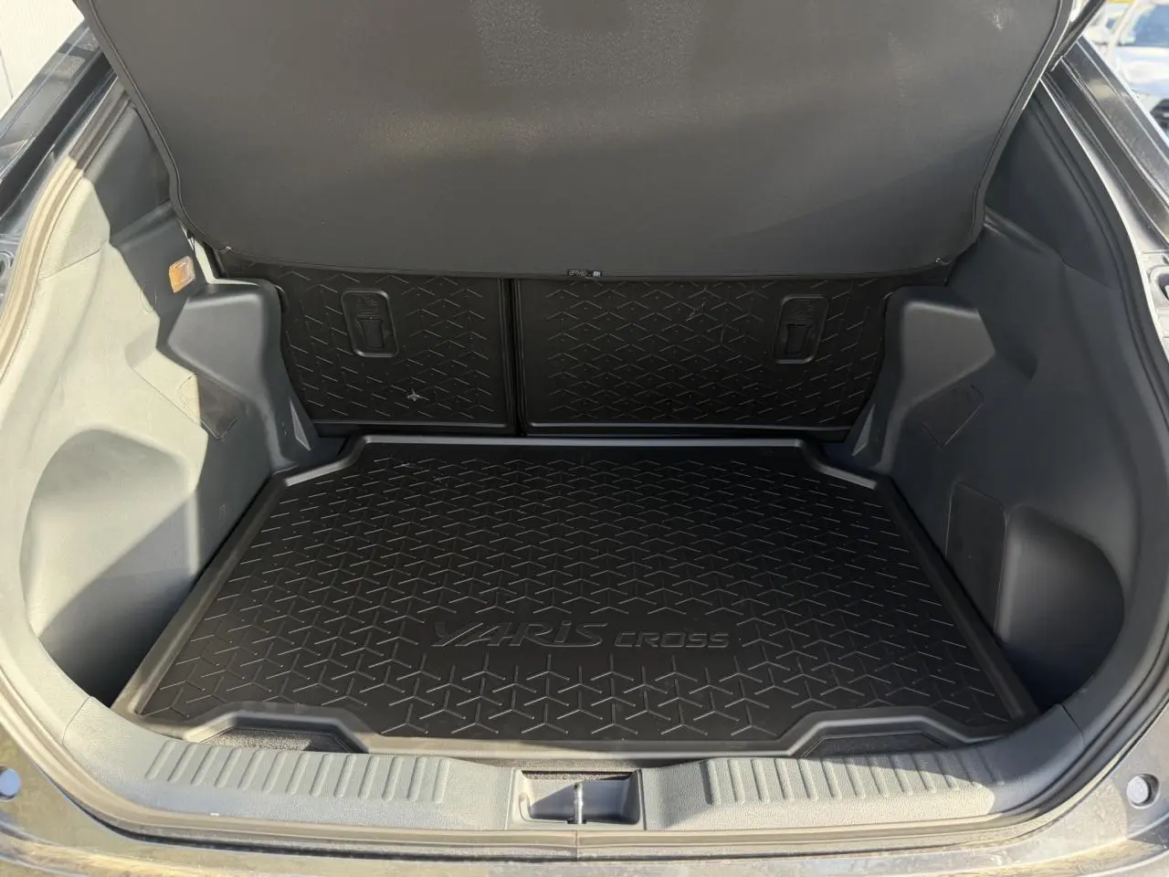 Coffre ouvert de Toyota Yaris Cross gris Atlas, vue plongeante sur tapis de coffre noir avec logo intégré.