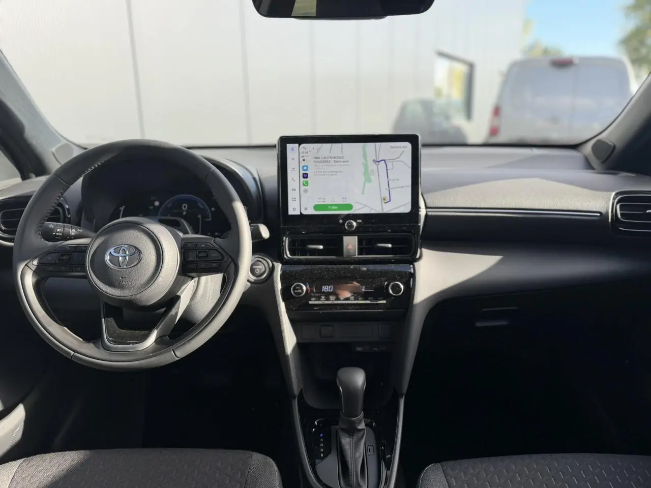Vue intérieure avant du Toyota Yaris Cross 2026, tableau de bord noir avec écran tactile GPS et volant multifonctions cuir.