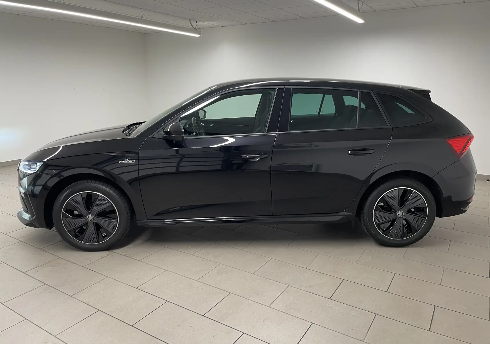 Vue de profil côté gauche d'une Skoda Scala 2025 noire métallisée avec jantes spécifiques Monte-Carlo et double plancher de coffre.