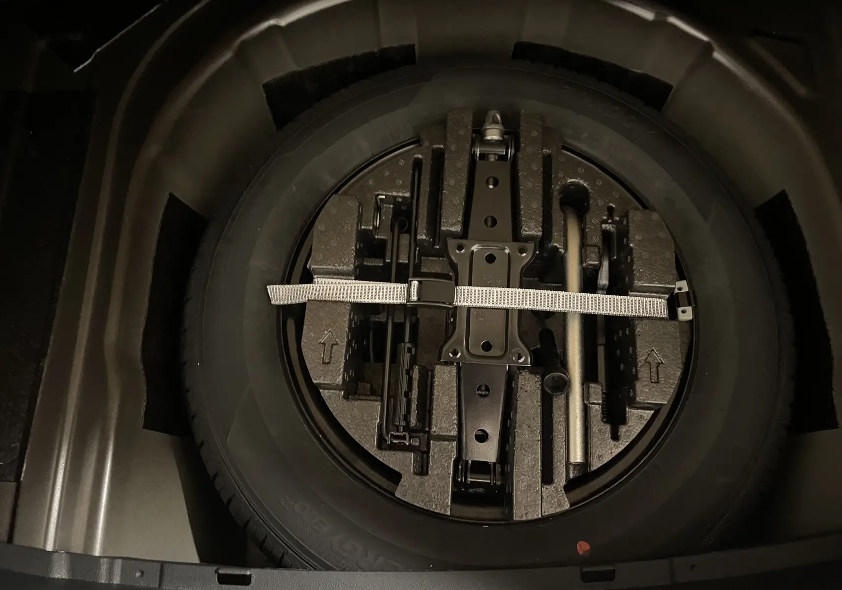 Gros plan sur la roue de secours et les outils de bord dans le double plancher du coffre du Skoda Scala Noir Magic.