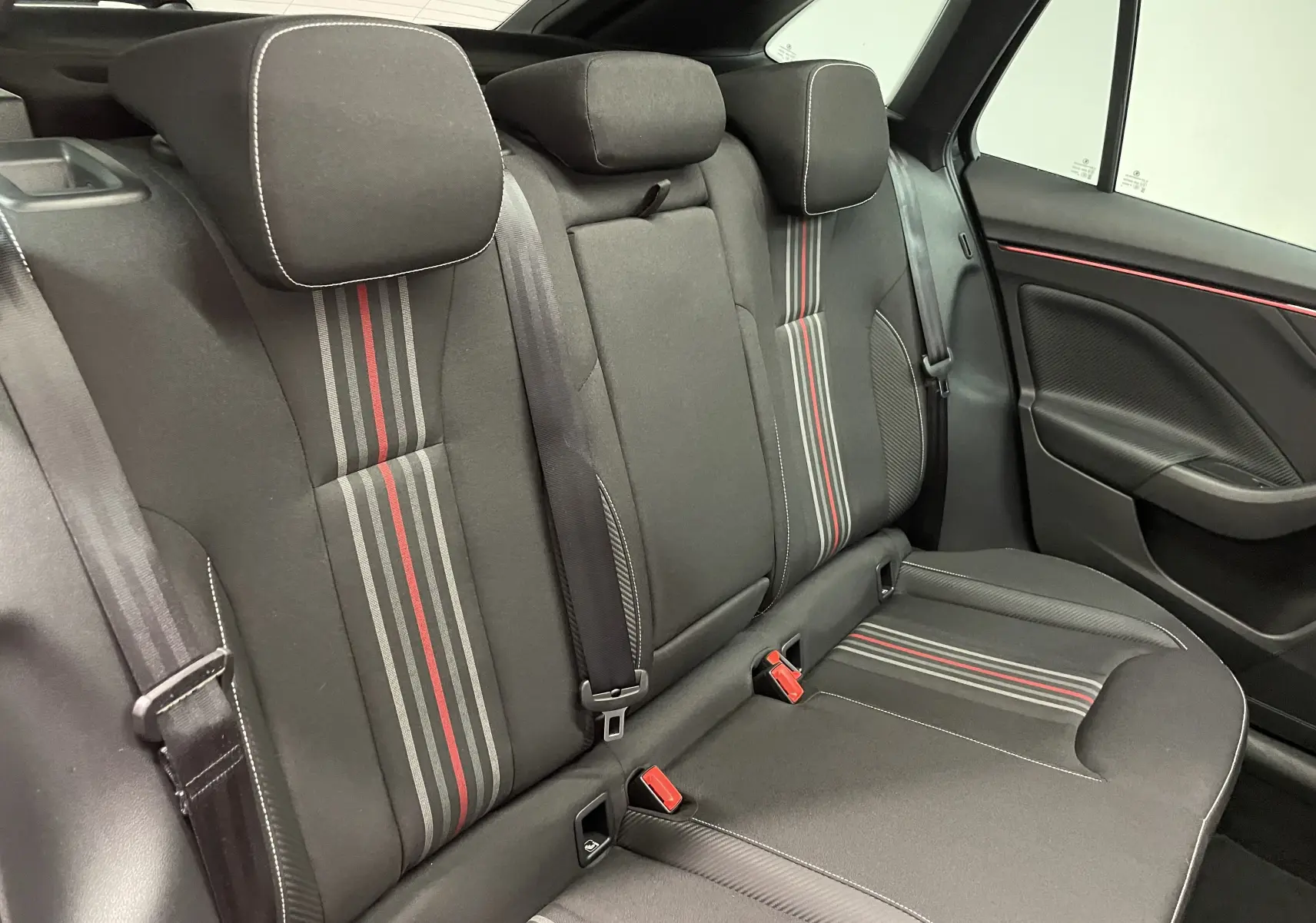 Vue intérieure des sièges arrière noirs avec bandes rouges et grises, et ceintures de sécurité dans une Skoda Scala 2025.