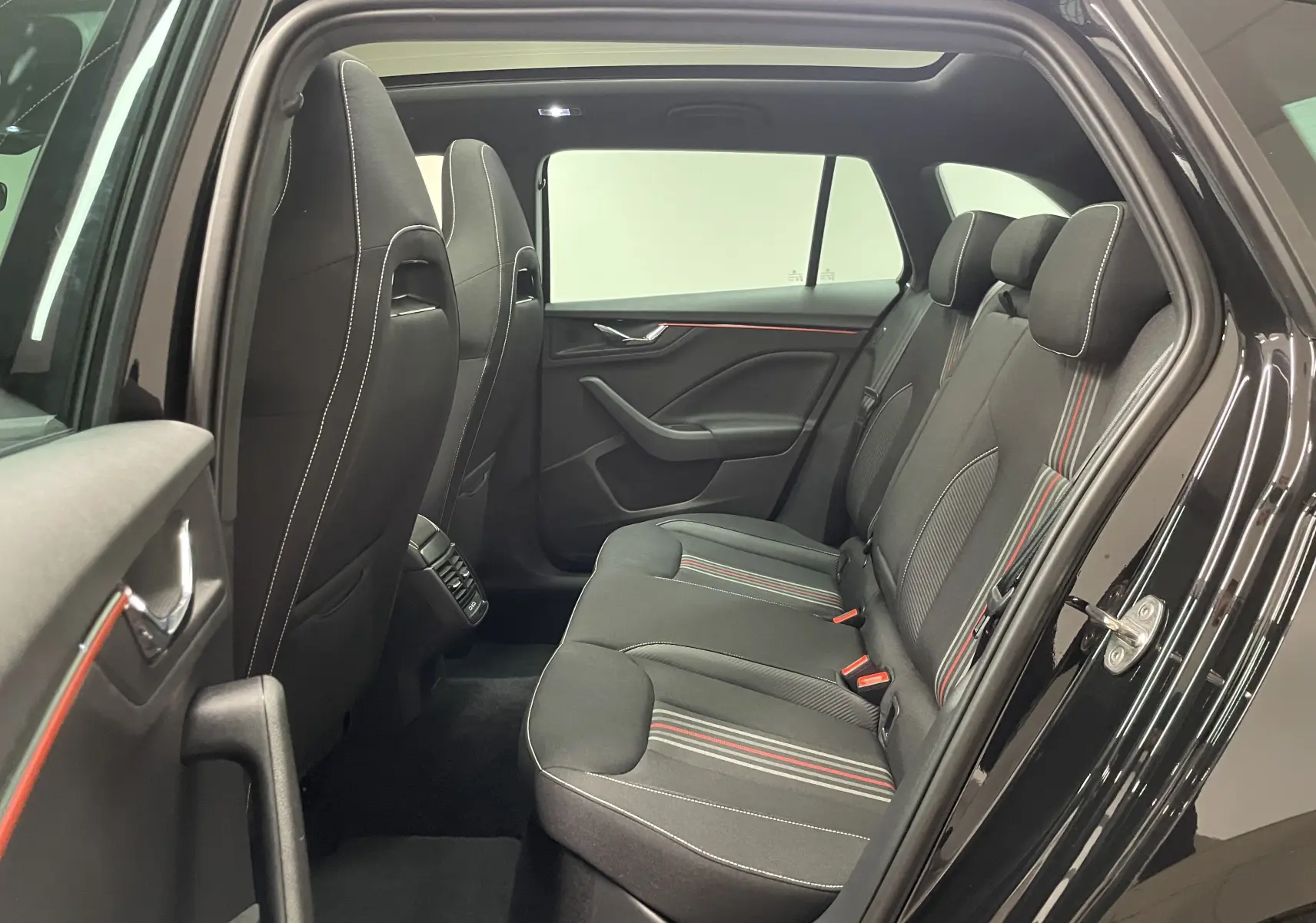 Vue intérieure côté droit sur les sièges arrière noirs avec surpiqûres blanches et bandes rouges du Skoda Scala Monte-Carlo 2025.