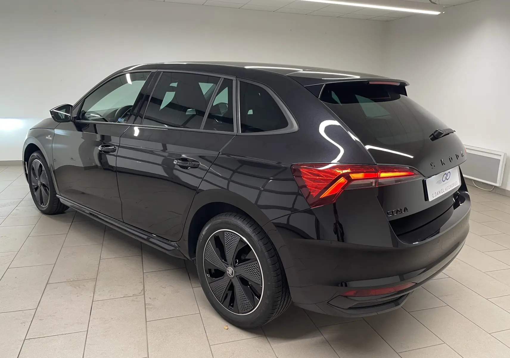 Vue 3/4 arrière droite d’une Skoda Scala 2025 Noir Magic avec feux arrière allumés et jantes spécifiques Monte-Carlo.