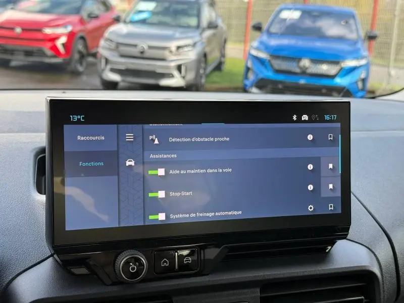 Vue intérieure centrée sur l'écran tactile du tableau de bord du Citroën Berlingo, avec voitures colorées visibles au loin.