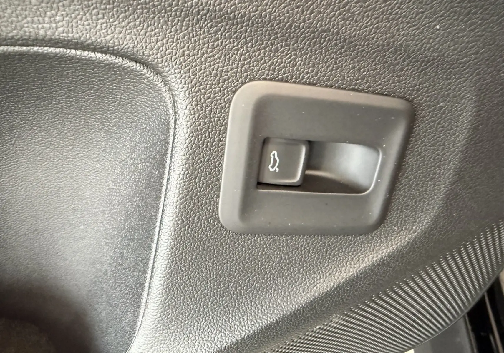 Gros plan sur le bouton d'ouverture du coffre intérieur en plastique noir texturé d'un Volkswagen T-Roc R-Line.
