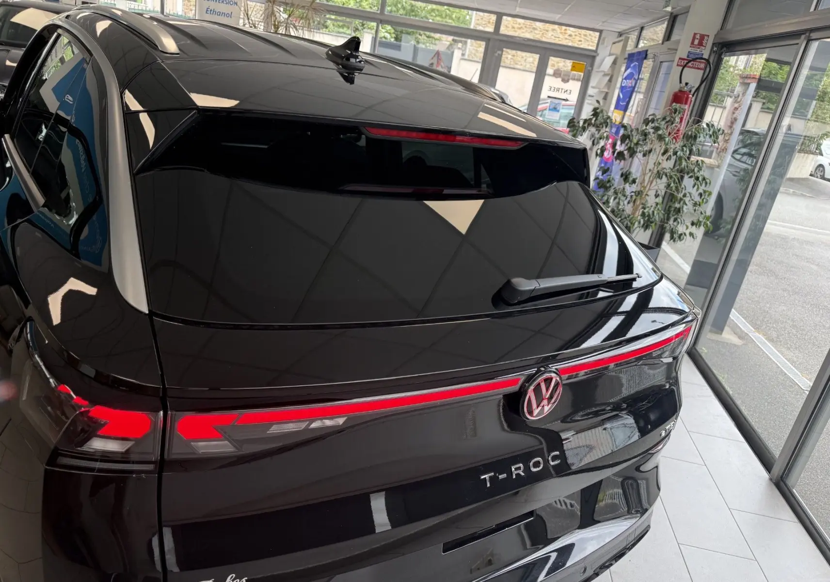 Vue 3/4 arrière du Volkswagen T-Roc R-Line noir intense avec feux arrière allumés en intérieur showroom.