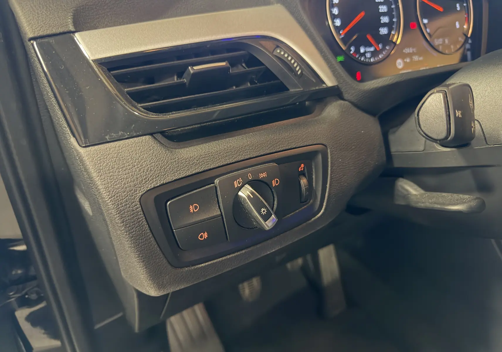Détail du tableau de bord côté gauche d’un BMW X1 noir 2019, avec commandes d’éclairage et partie du compteur visible.