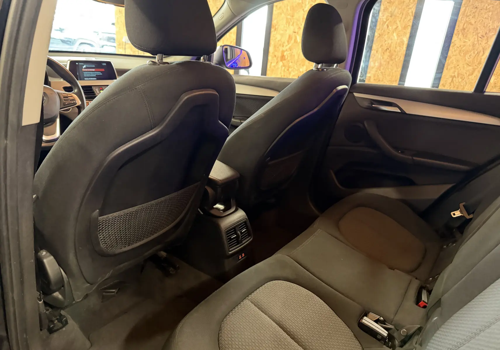 Vue intérieure arrière côté gauche du BMW X1 noir 2019, montrant les sièges avant et arrière en tissu avec aérateurs centraux.