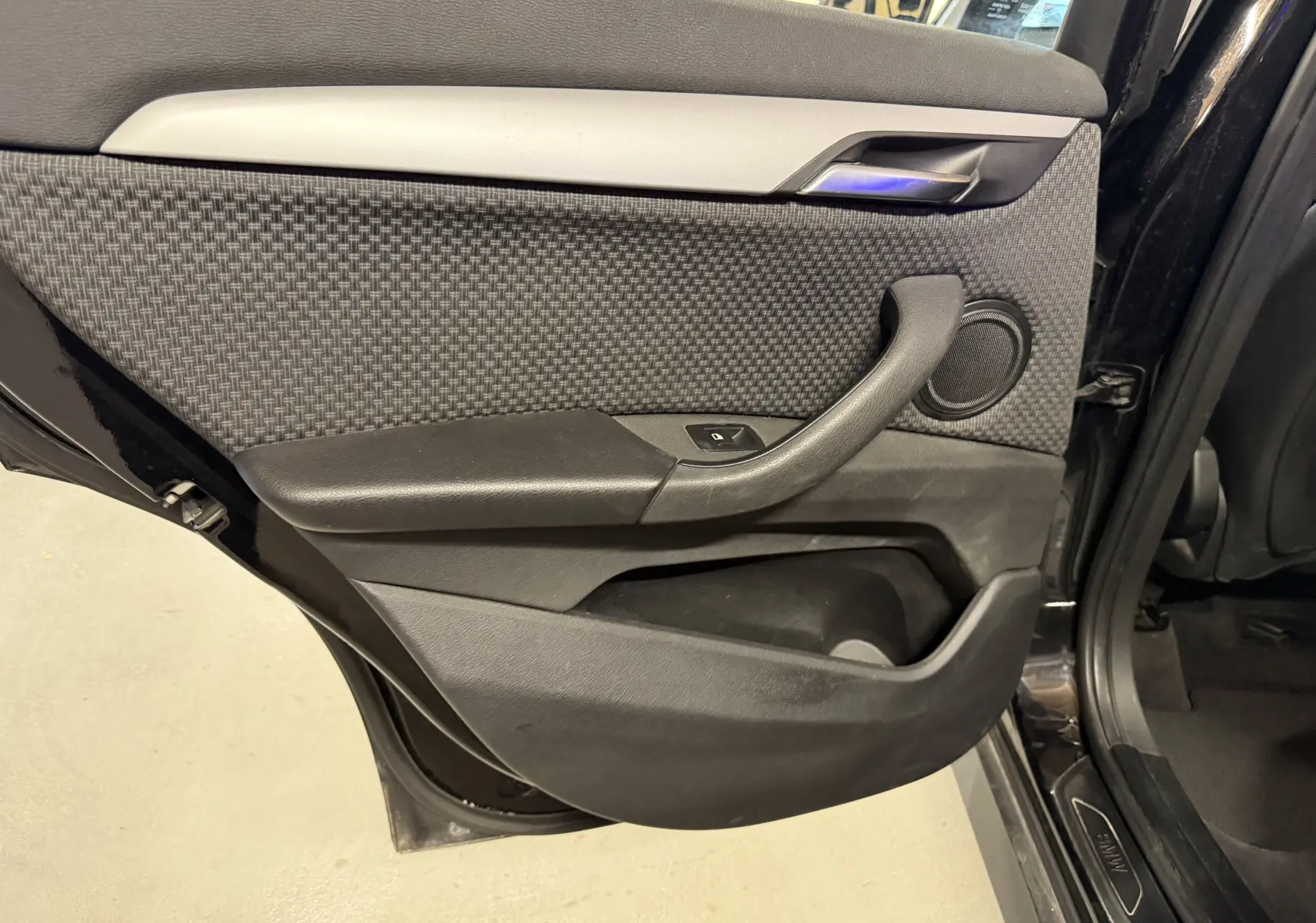 Porte arrière gauche ouverte d'une BMW X1 noire 2019, montrant le revêtement tissu et plastique avec commande de fenêtre.