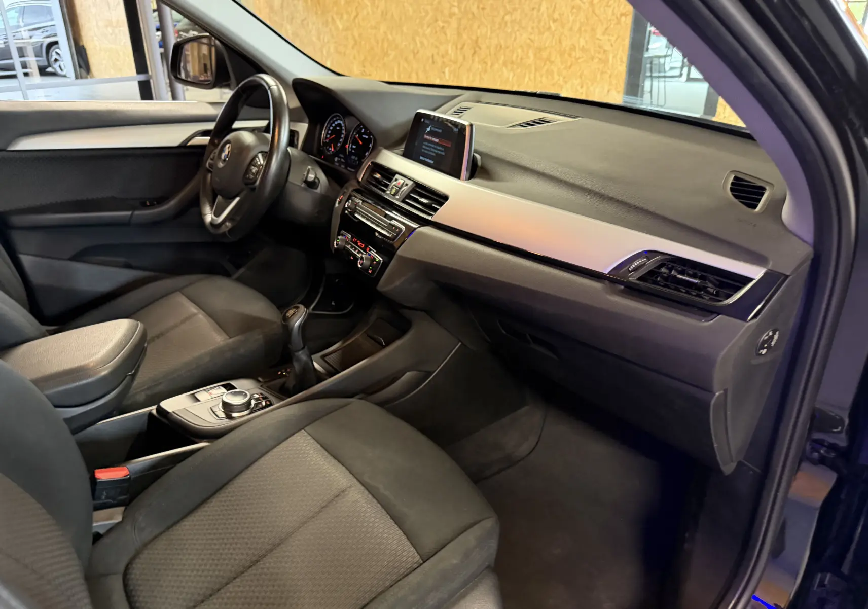 Vue intérieure côté conducteur de la BMW X1 noire 2019, montrant le tableau de bord et la boîte manuelle.