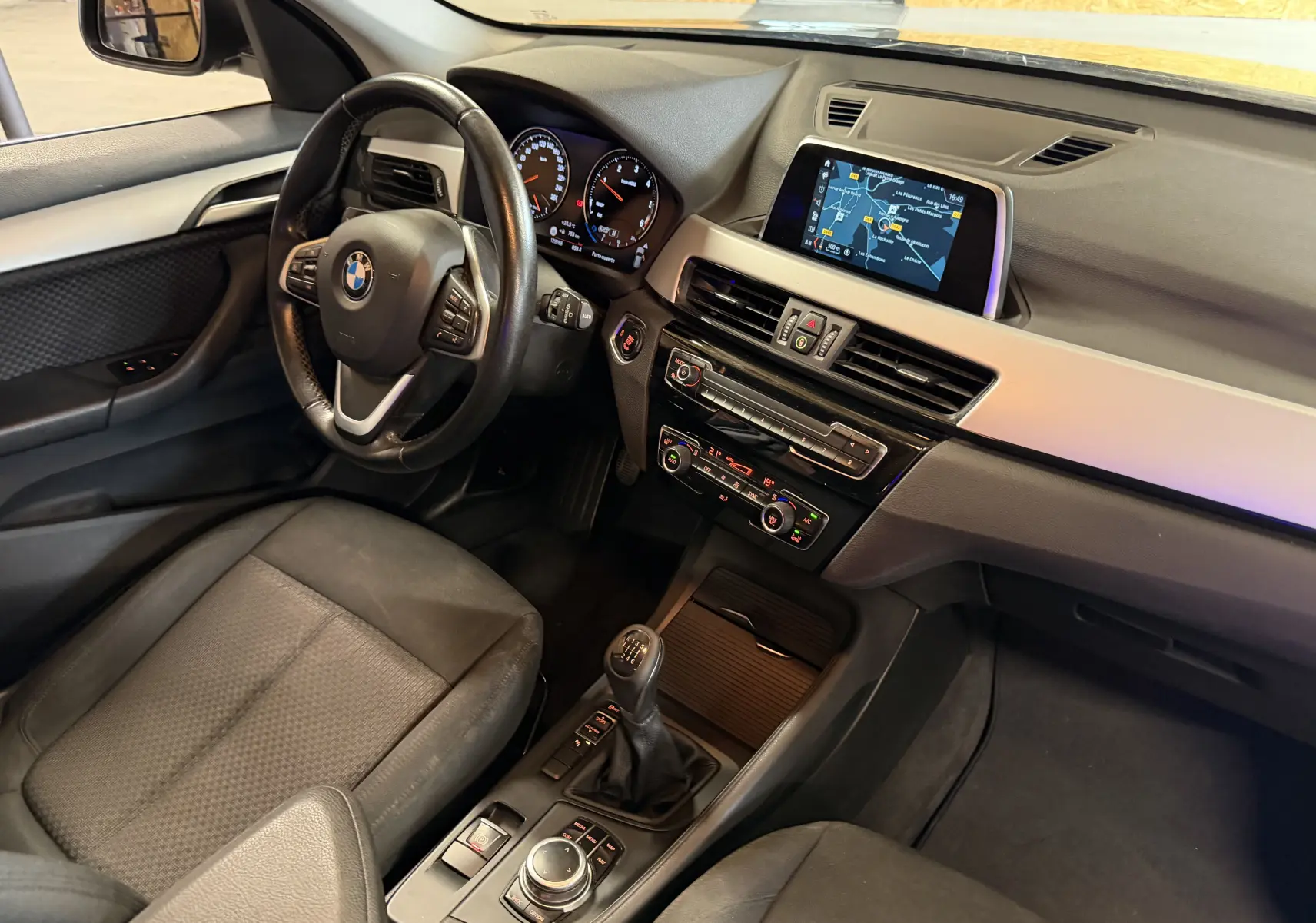 Vue intérieure côté conducteur de la BMW X1 noire 2019, mettant en valeur le volant, la console centrale et l'écran tactile avec navigation.