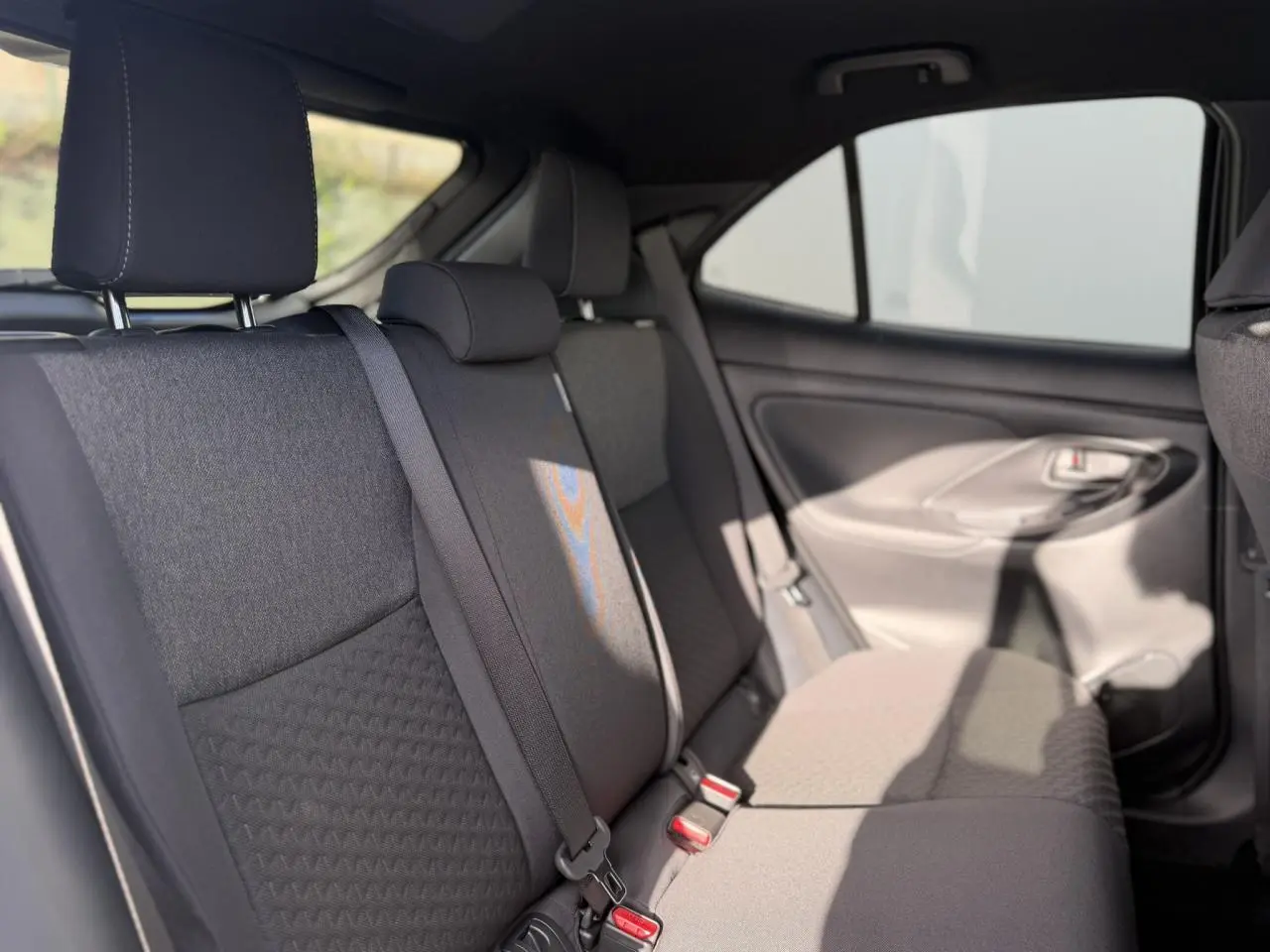 Vue intérieure sur les sièges arrière gris foncé de la Toyota Yaris Cross 2026 avec ceinture de sécurité et ciel de toit noir.