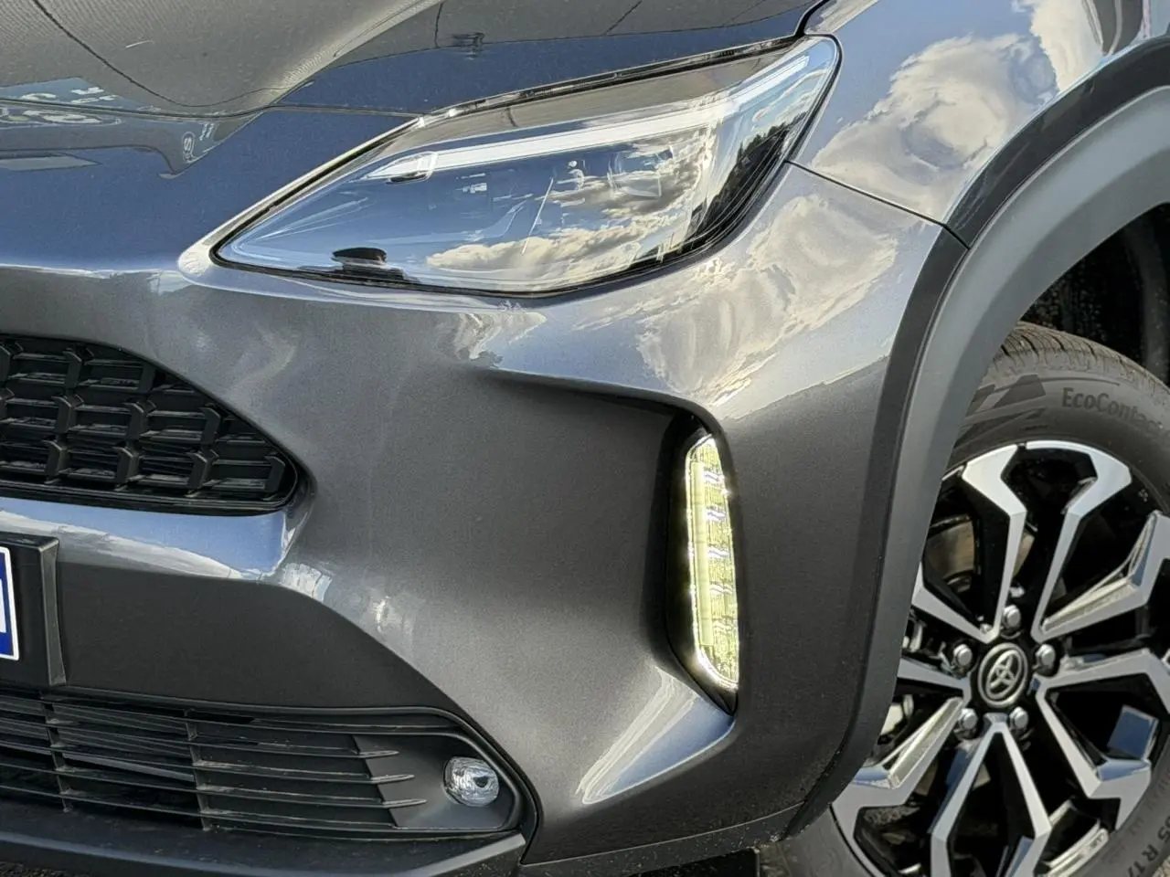 Gros plan sur l'avant droit gris Atlas du Toyota Yaris Cross 2026, mettant en valeur le phare LED et la jante alliage 17 pouces.