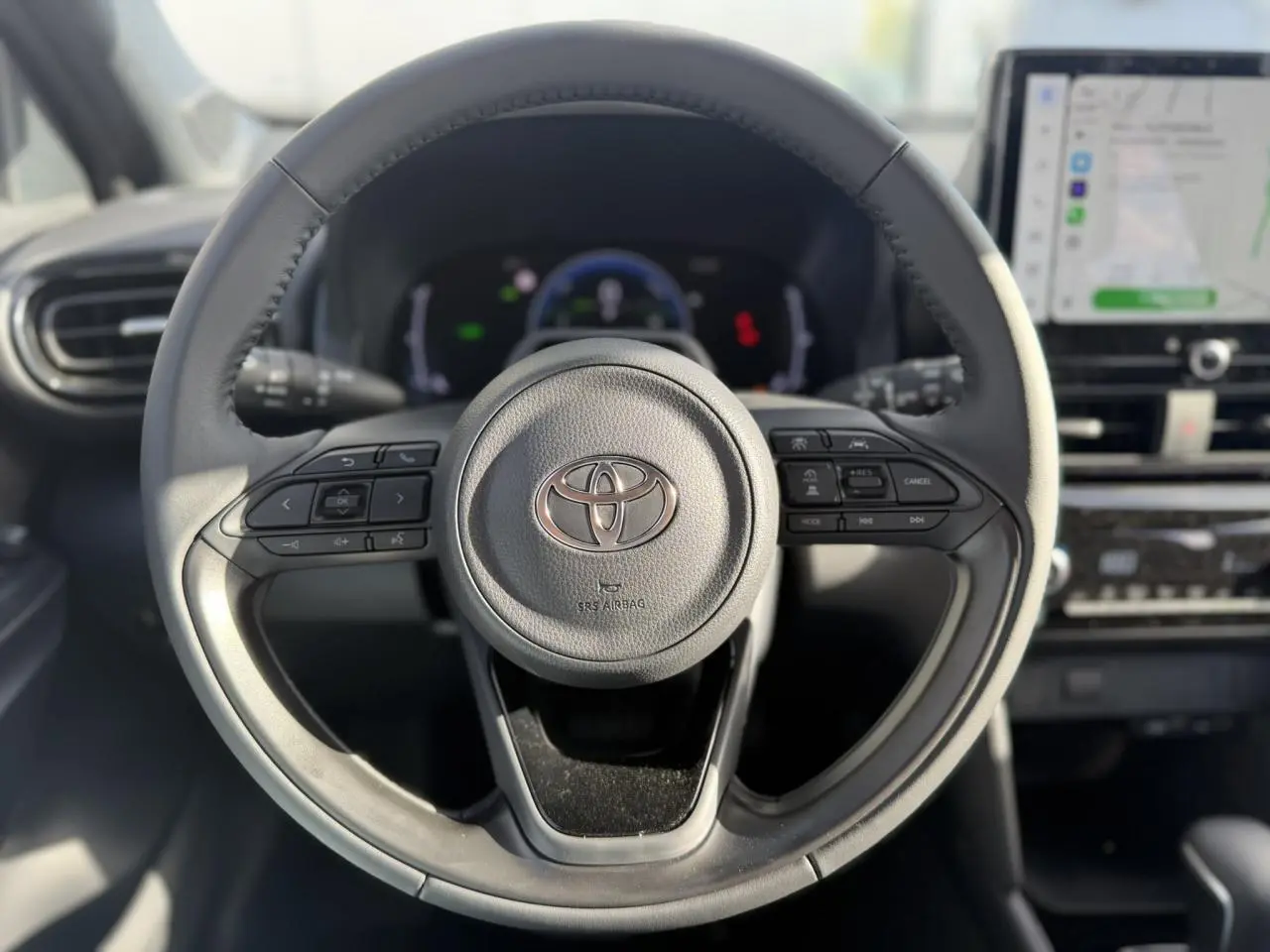 Vue rapprochée du volant multifonctions en cuir de la Toyota Yaris Cross 1.5 Hybrid 130 BVA Design, avec tableau de bord et écran tactile.
