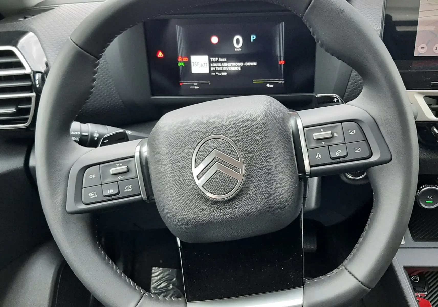 Vue rapprochée du volant noir de la Citroën C4 1.2 Hybrid 2026 avec tableau de bord digital affichant la radio TSF Jazz.