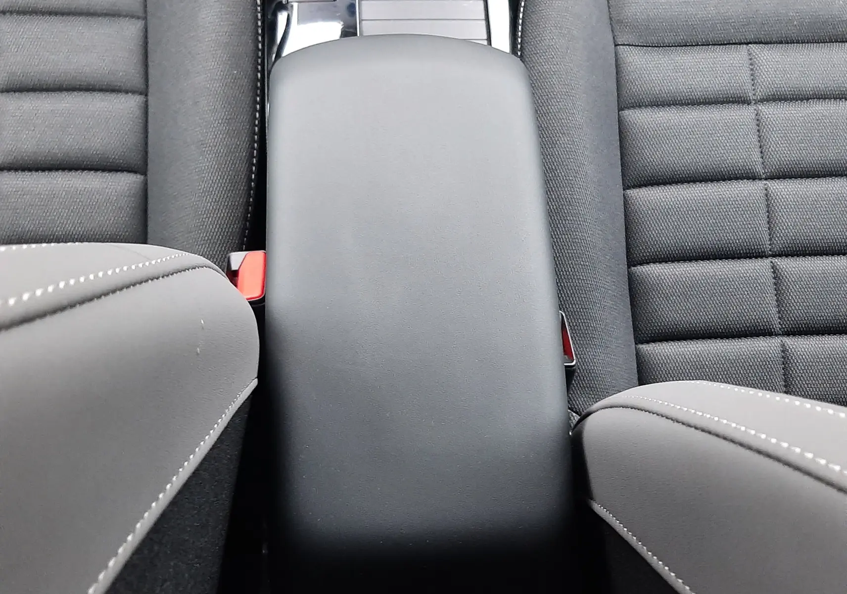 Vue intérieure centrée sur l'accoudoir noir entre les sièges avant gris foncé du Citroën C4 hybride 2026.