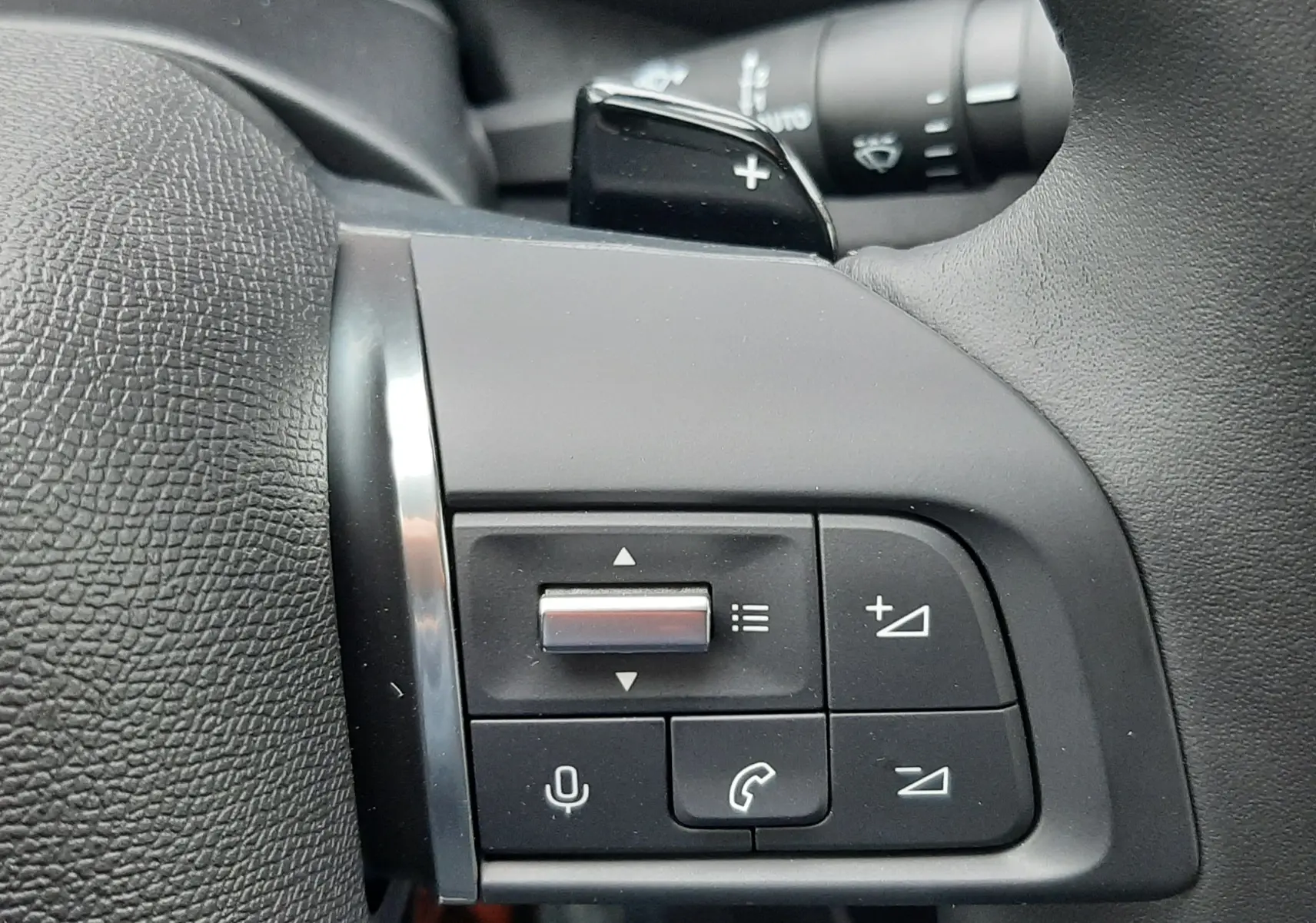 Gros plan sur les commandes multifonctions noires à gauche du volant en cuir noir du Citroën C4 hybride blanc.