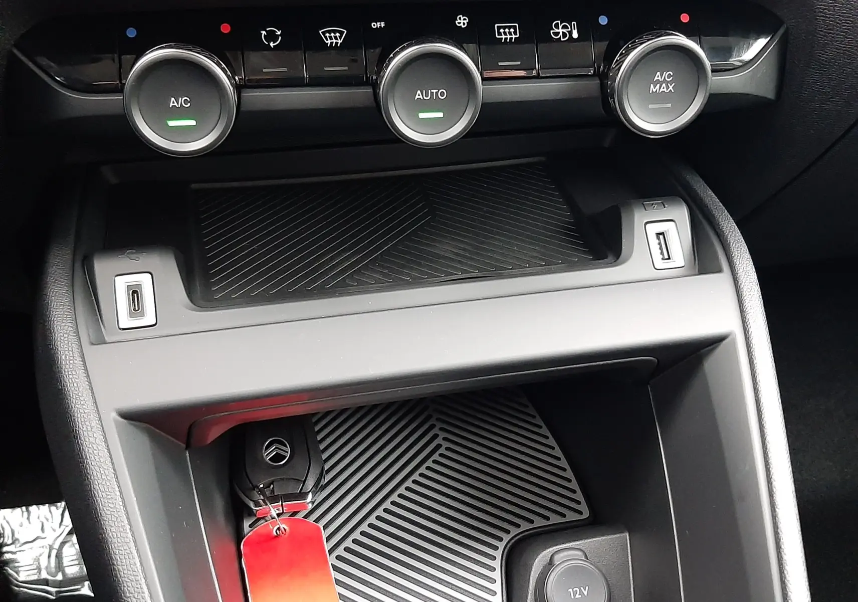 Détail de la console centrale de la Citroën C4 hybride blanche, avec commandes climatisation et prise 12V visibles.