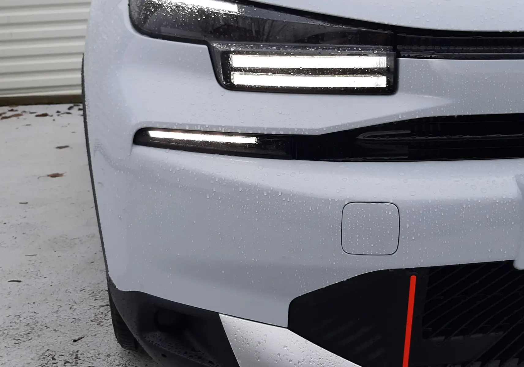 Gros plan sur l'avant gauche blanc Okenite d'une Citroën C4 1.2 Hybrid 145ch avec phares LED allumés sous la pluie.