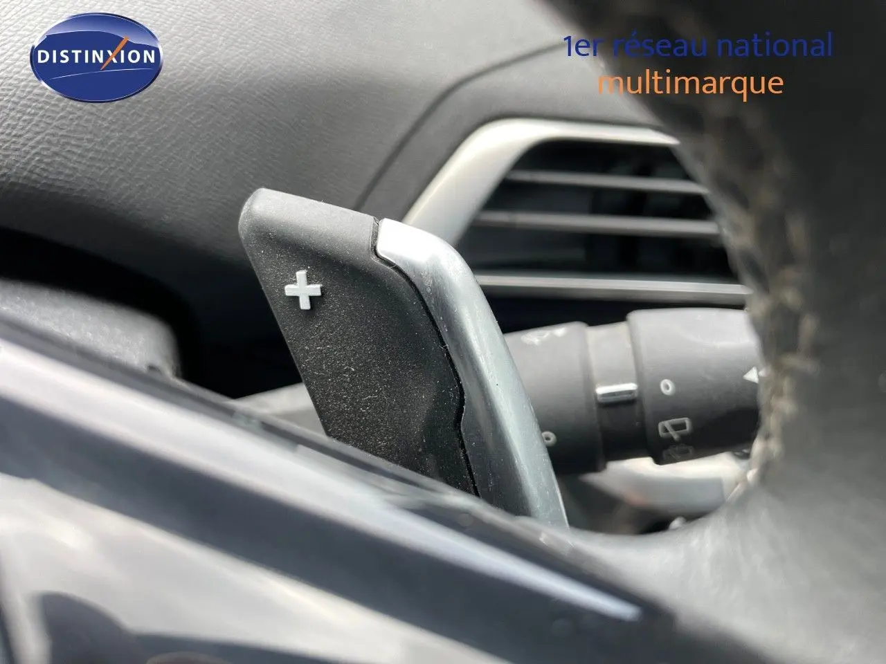 Gros plan sur la palette de changement de vitesse "+" derrière le volant d'un Peugeot 3008 gris, intérieur noir.