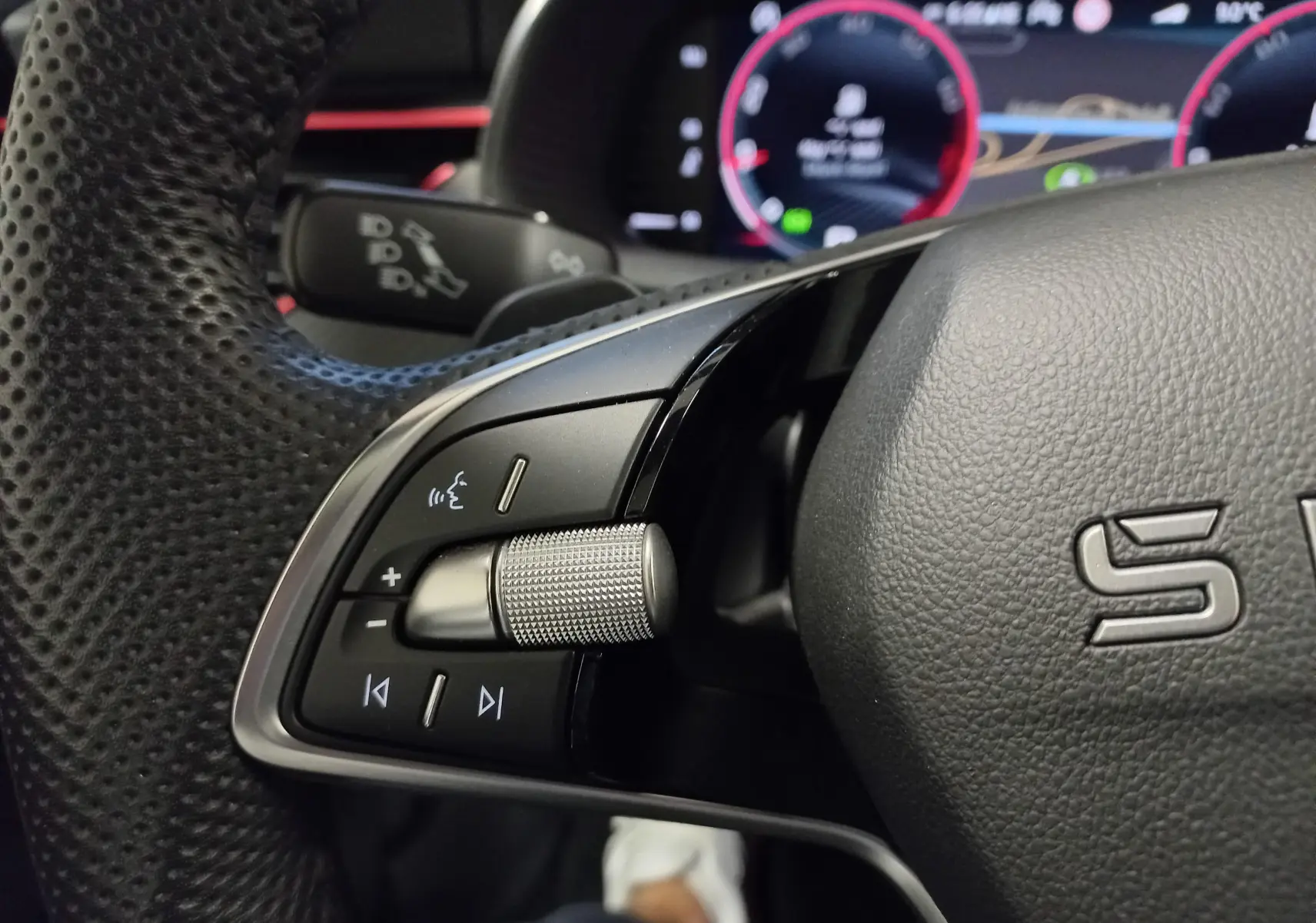 Gros plan sur la commande gauche du volant perforé d'une Skoda Scala 2025 avec tableau de bord numérique en arrière-plan.