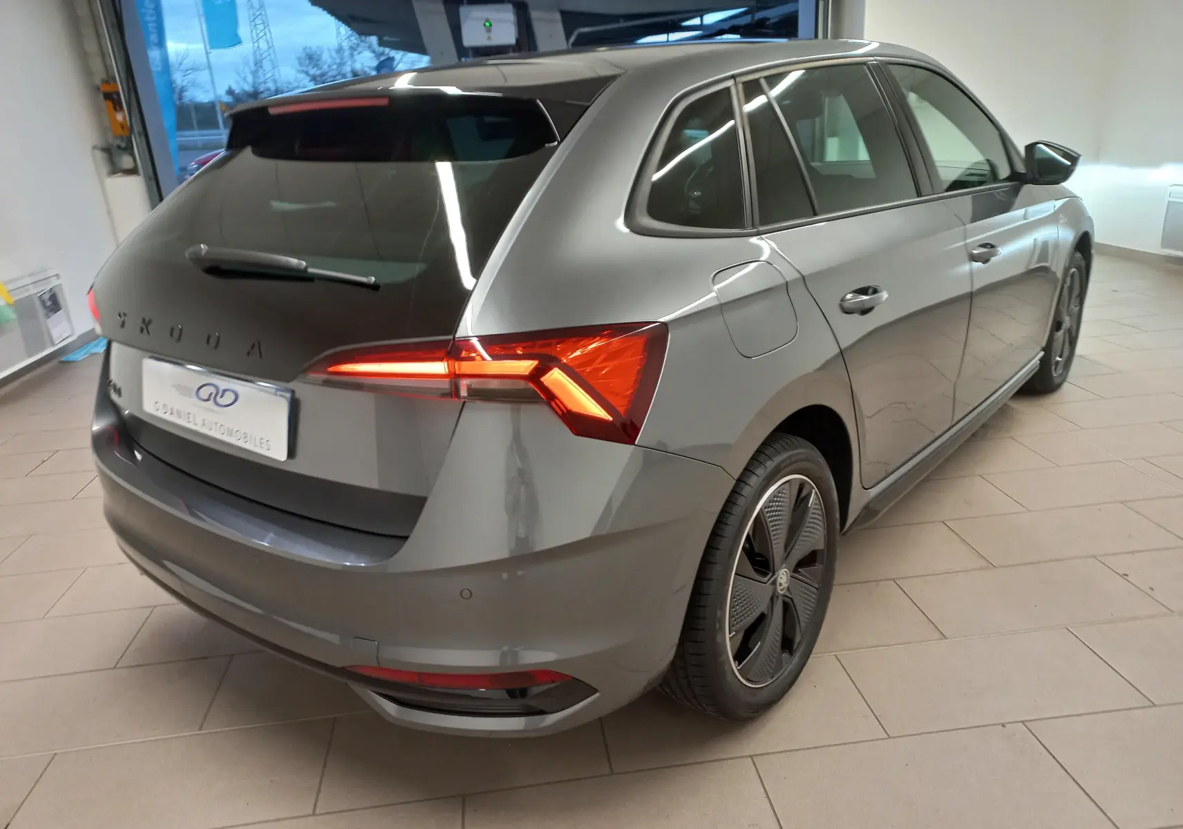 Vue 3/4 arrière droite d'une Skoda Scala 1.5 TSI Monte-Carlo gris graphite avec feux arrière allumés en intérieur showroom.