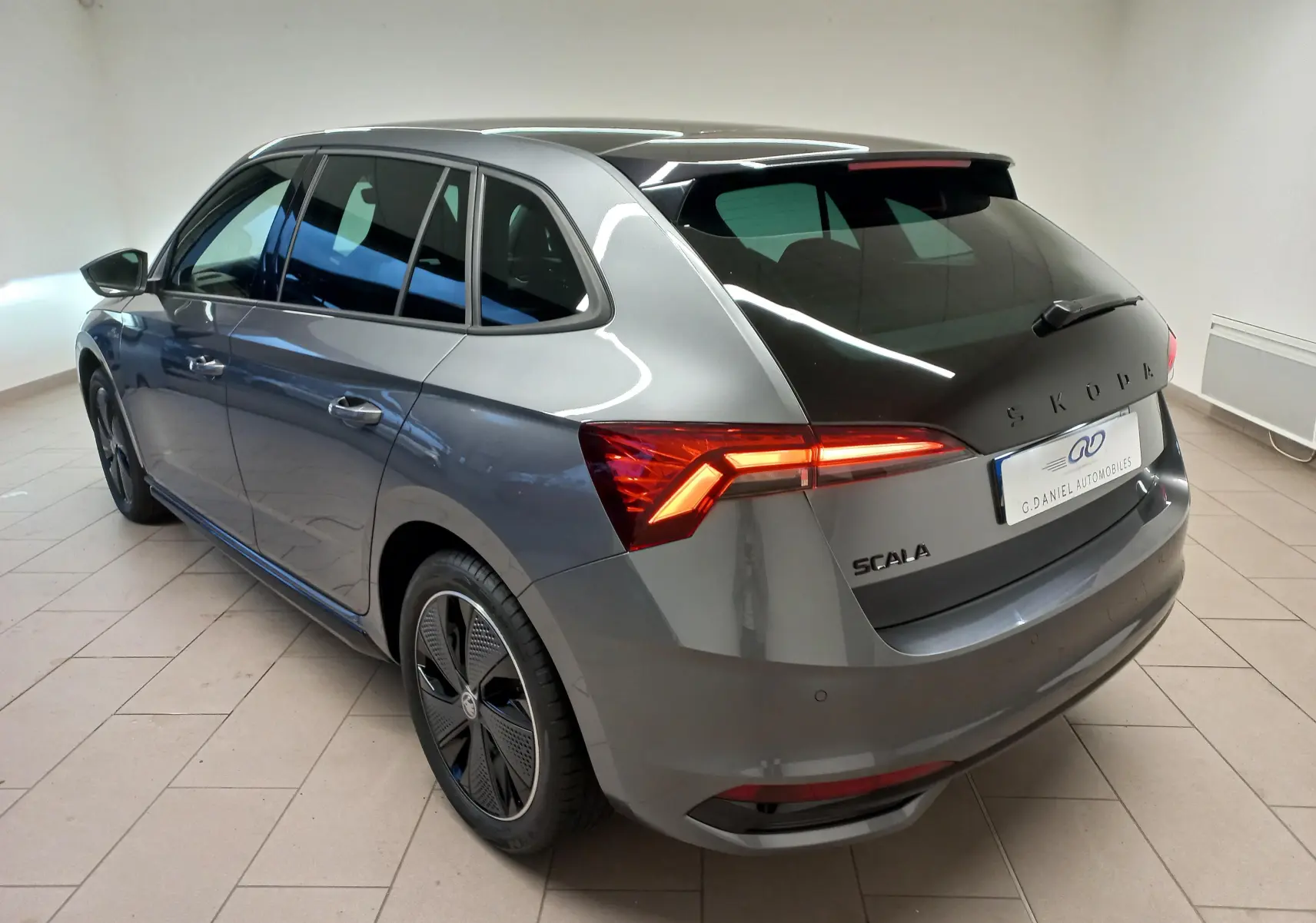 Vue 3/4 arrière droite d'une Skoda Scala 1.5 TSI Monte-Carlo gris graphite avec feux arrière allumés en intérieur showroom.