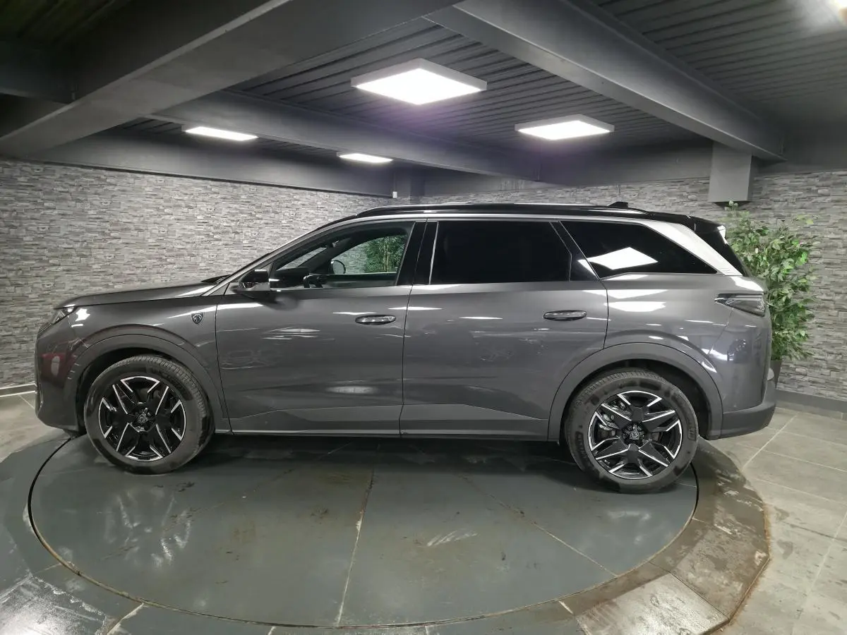 Vue de profil côté gauche d’un Peugeot 5008 gris métallisé avec jantes alliage noires dans un showroom intérieur.