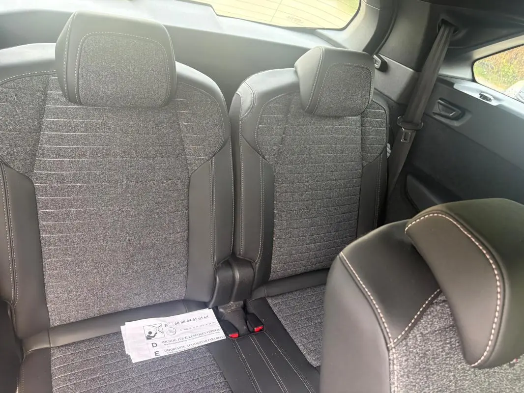 Vue intérieure sur les sièges arrière du Peugeot 5008 Hybrid 2025, tissu gris et cuir noir avec surpiqûres blanches.