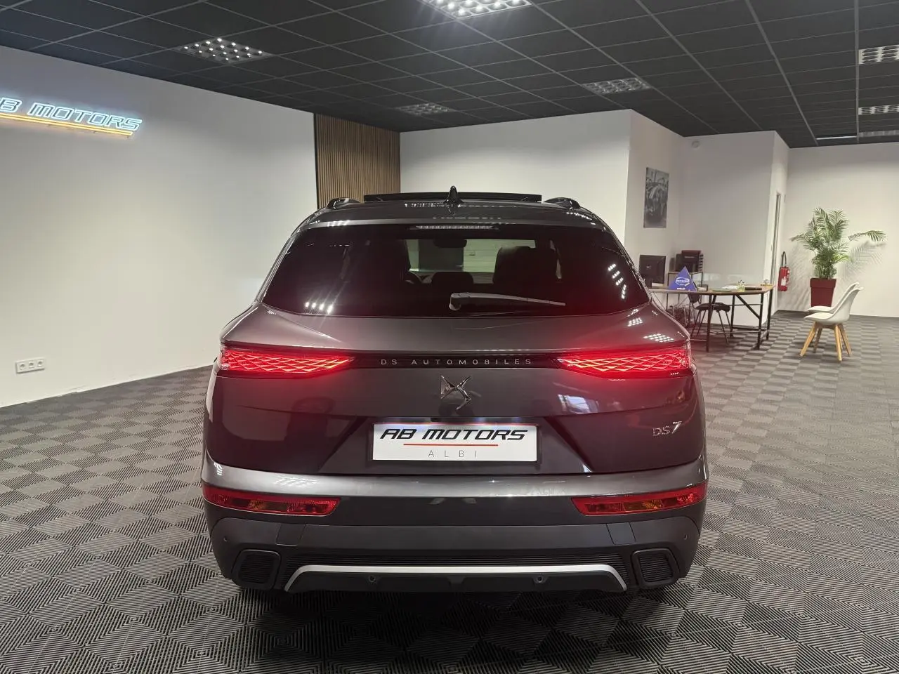 Vue arrière d'un DS7 Crossback gris métallisé avec feux arrière LED 3D allumés dans un showroom.