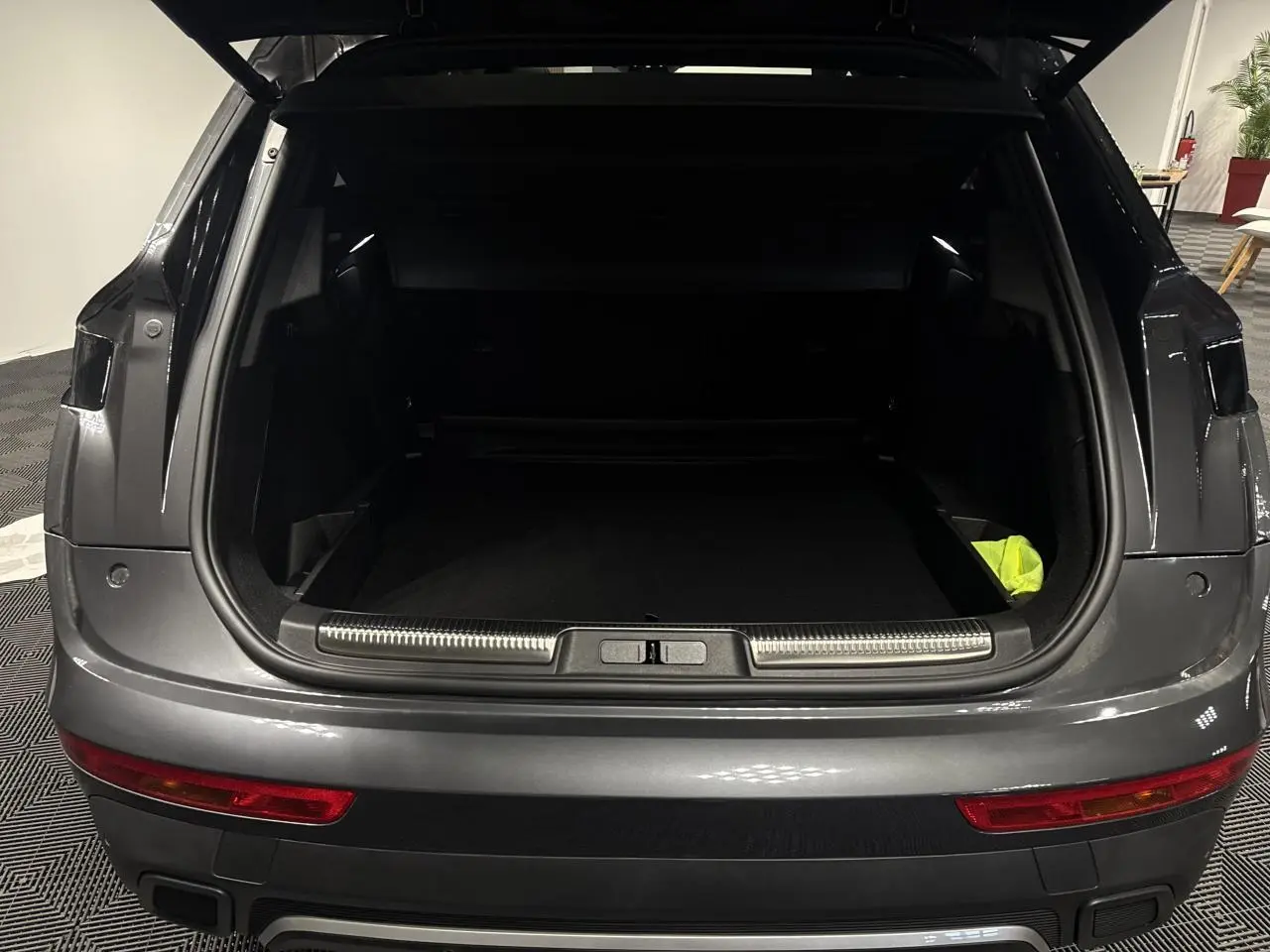 Vue arrière du coffre ouvert d’un DS7 Crossback gris métallisé, montrant l’espace de chargement et le pare-chocs avec feux rouges.