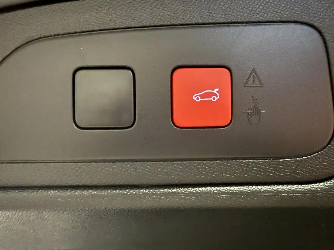 Gros plan sur le bouton rouge d'ouverture du hayon dans l'habitacle du DS7 Crossback gris 2025.