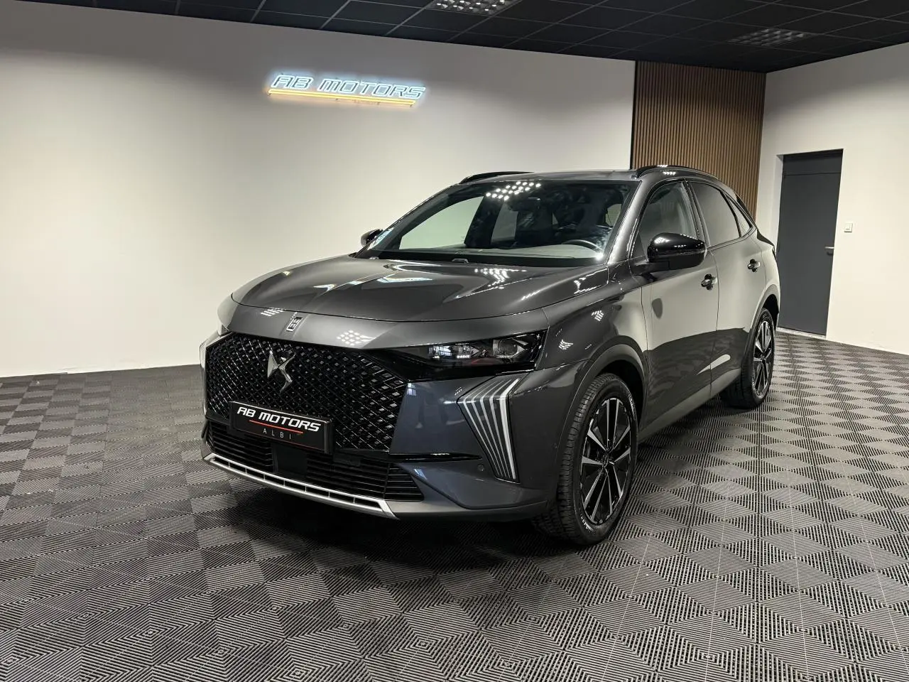 DS7 Crossback gris en 3/4 avant droit, avec calandre noire brillante et jantes alliage 19 pouces distinctives.