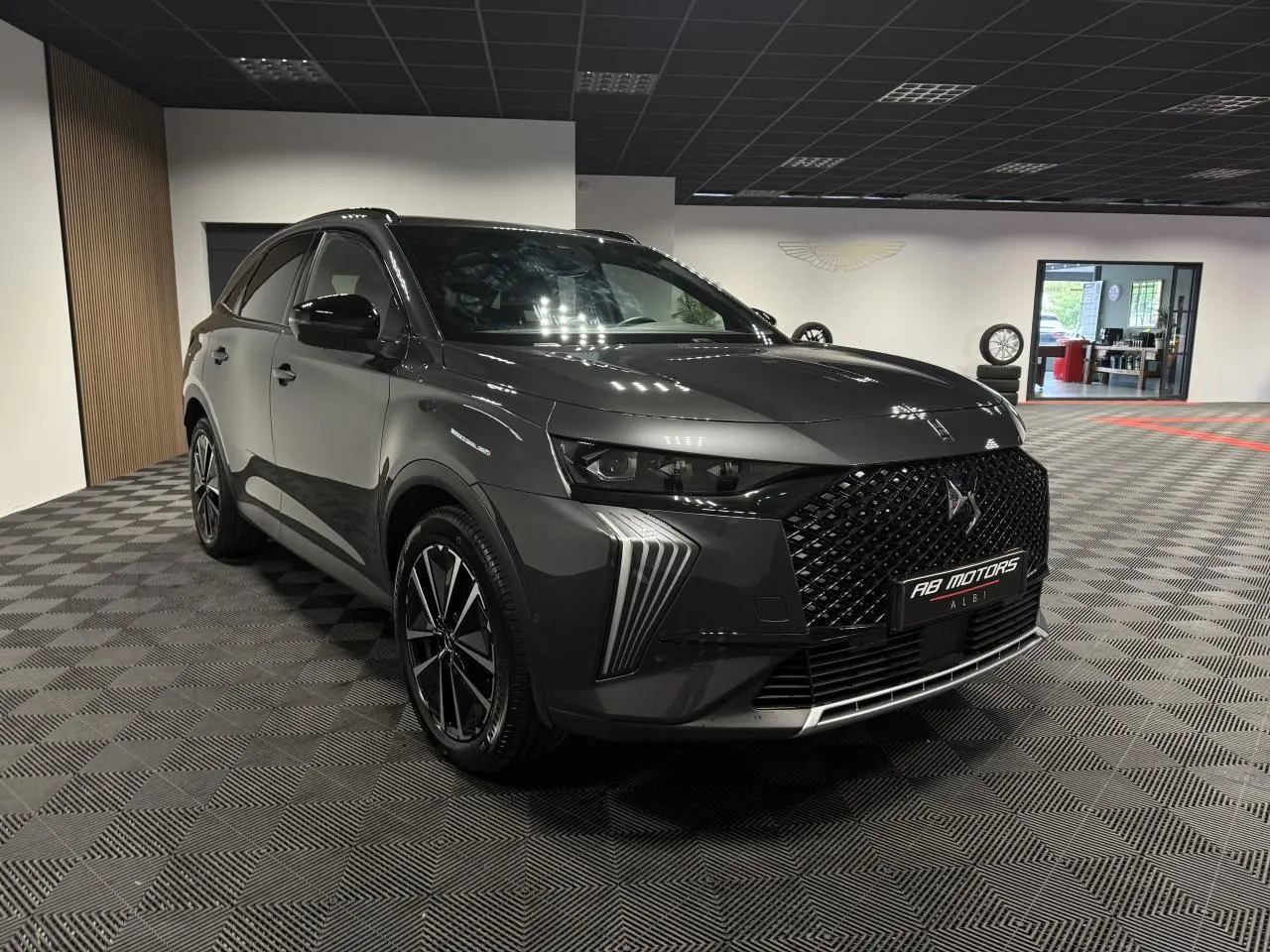 DS7 Crossback gris en 3/4 avant droit, avec calandre noire brillante et jantes alliage 19 pouces dans un showroom.